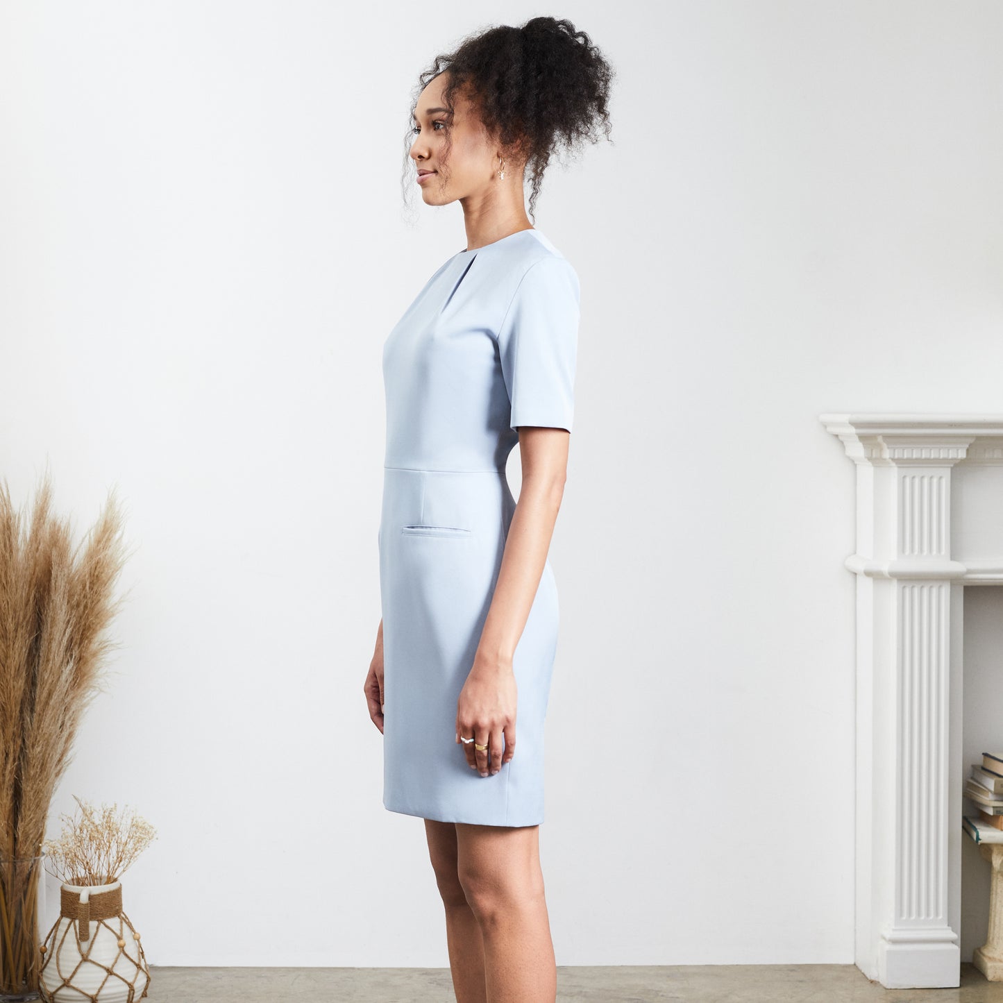 Side view blue sheath dress worn by a brown skinned woman with curly hari in a ponytail